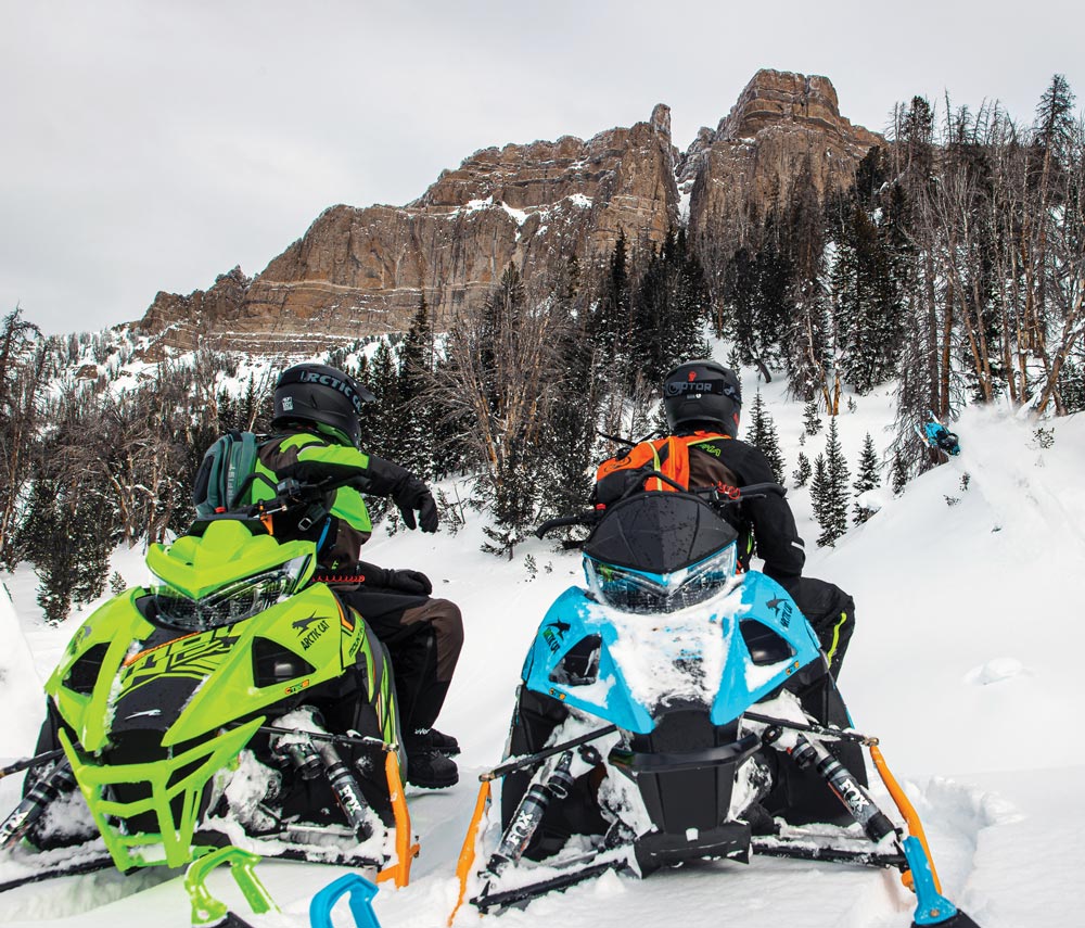 Two riders on snowmobiles looking at mountain